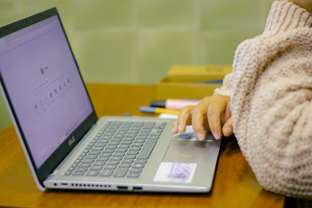 Close-up of a student using a laptop with stationery on a wooden desk in a cozy indoor setting.